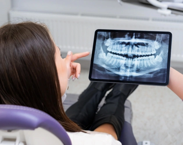 Dental professional examining panoramic X-ray on tablet in clinical setting.
