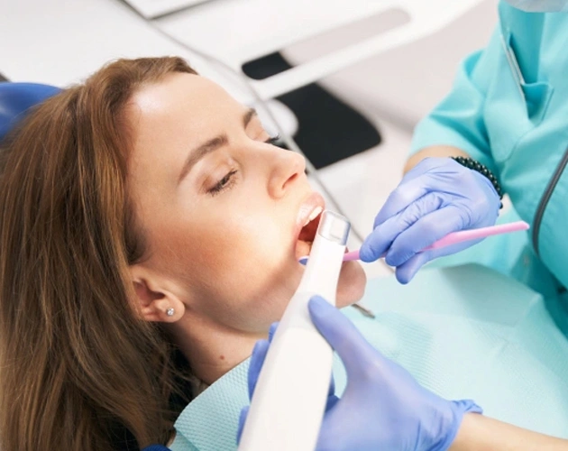 Woman receiving dental examination from gloved dentist in clinical setting.