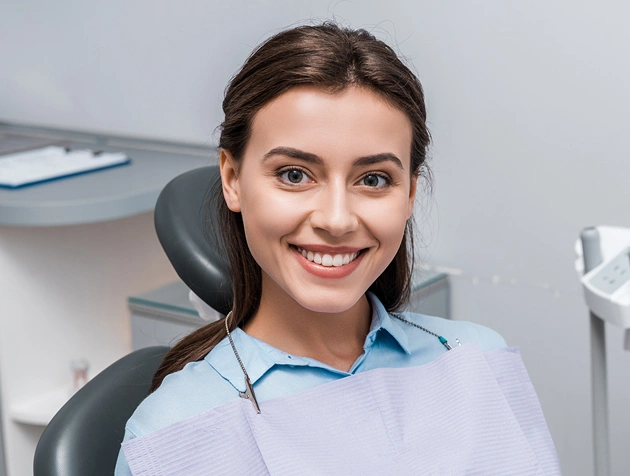 Smiling dental professional in light blue scrubs seated in modern dental office chair.