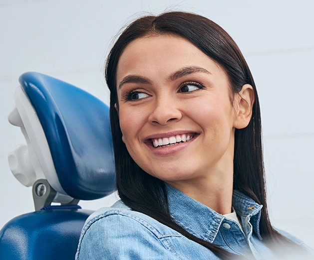 Smiling woman in dental chair at periodontal office, looking toward camera confidently.