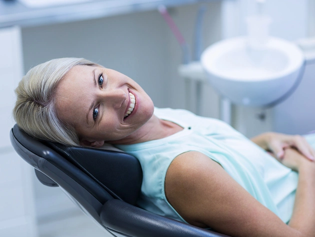 Patient reclined in dental chair smiling during periodontal examination at dental office.