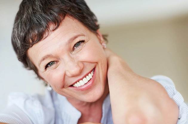 Woman with short dark hair smiling warmly in casual setting, dental practice promotional photo.