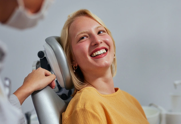 Smiling woman in yellow shirt holding dental mirror tool against white background.