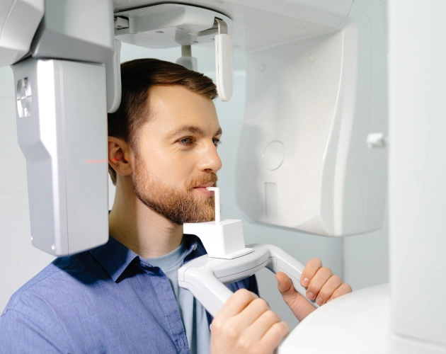 Male dentist operating dental imaging equipment in modern clinical setting.
