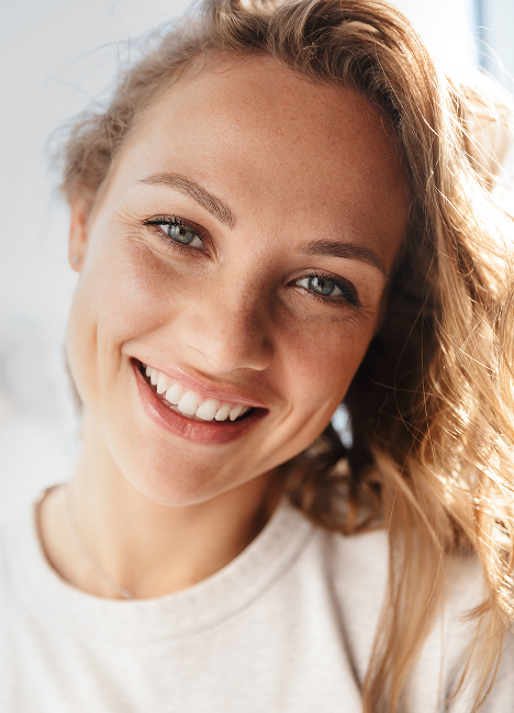 Smiling young woman with reddish-blonde hair against white background, dental office portrait.
