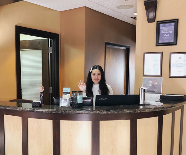Receptionist at dental office front desk with computer in professional clinical setting.