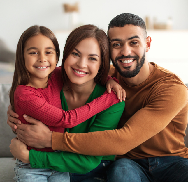 Happy family of three smiling together indoors, embracing in casual clothing.