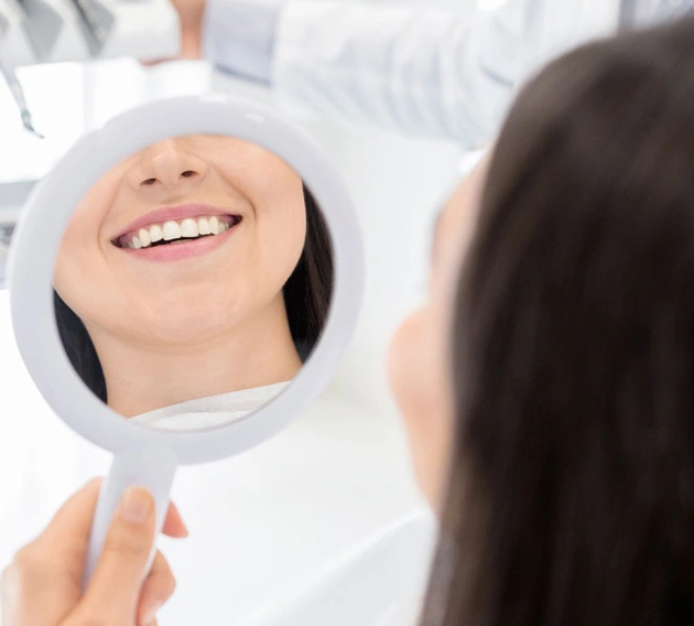 Woman smiling at reflection in hand mirror, showing healthy teeth and gums.