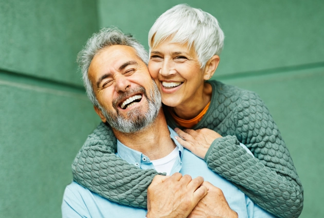Happy mature couple smiling together against green background, embracing with affection.