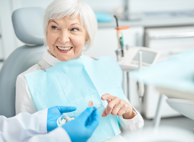 Senior woman smiling in dental chair, holding blue bib in modern periodontal office.