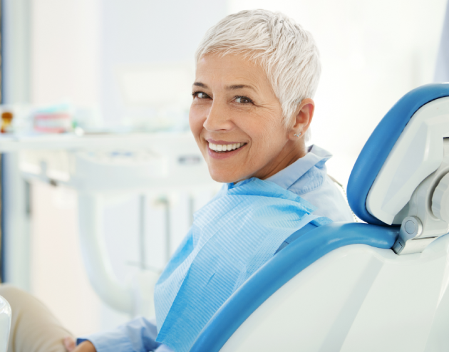 Smiling woman in dental chair wearing blue bib in modern periodontal office setting.