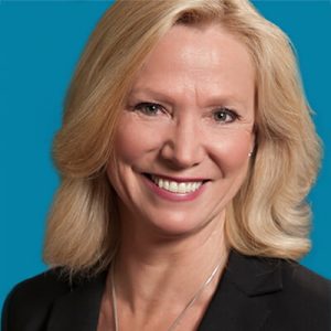 Professional headshot of blonde woman smiling against blue background, dental practice staff portrait.