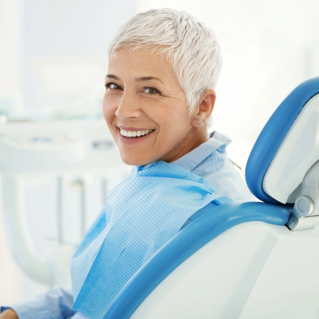 Smiling woman in dental chair wearing blue bib at periodontal practice office