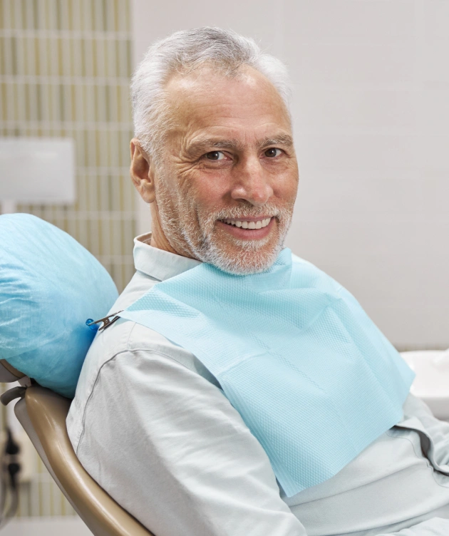 Smiling male patient wearing blue bib in dental chair at periodontal office.