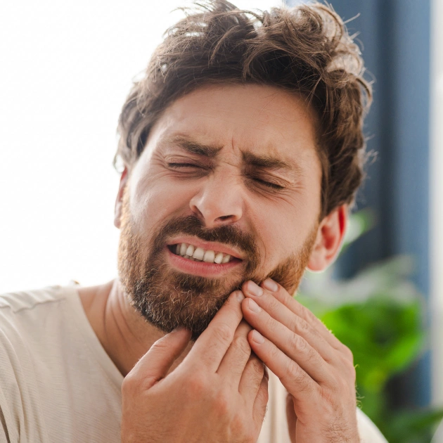 Man experiencing tooth pain, holding jaw with hand outdoors during daytime.