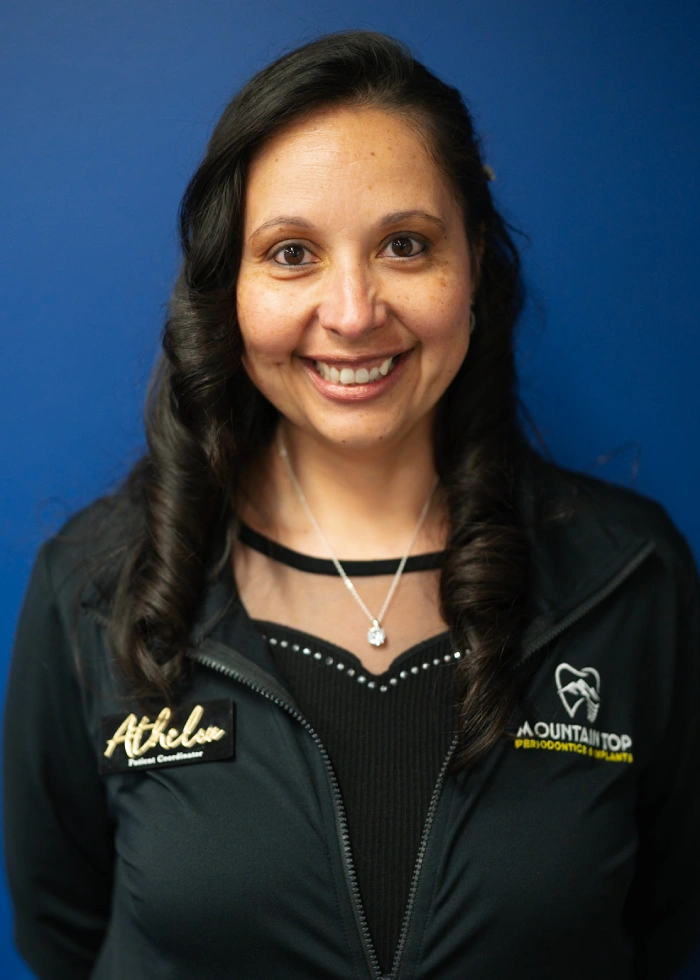 Professional headshot of smiling woman in dark jacket against blue background, dental practice staff portrait.
