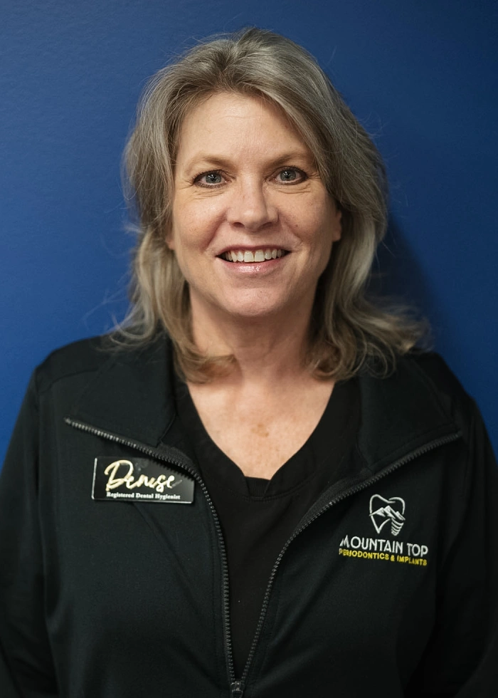 Professional headshot of woman in black jacket against blue background for dental practice.