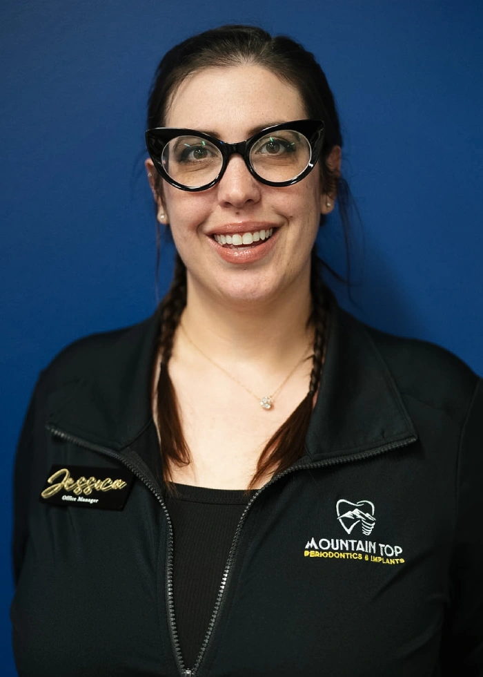 Professional woman wearing glasses and black jacket with Mountain Top Periodontics logo against blue background.