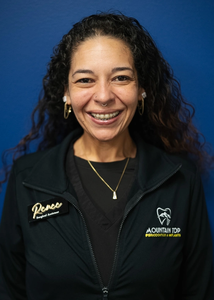 Professional headshot of woman smiling against blue background, wearing black jacket with dental practice logo.