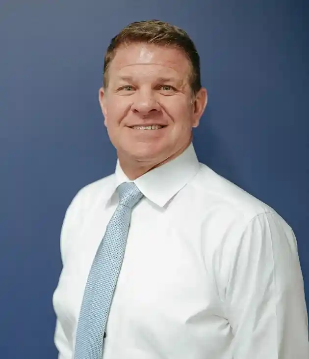 Professional headshot of male dental professional wearing white shirt and gray tie against blue background.