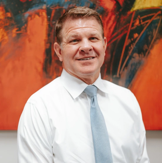 Professional headshot of man in white shirt and blue tie against colorful abstract background.