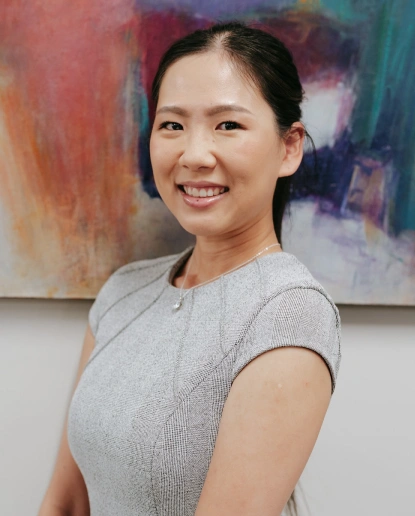 Professional headshot of smiling woman in gray shirt against colorful abstract background.