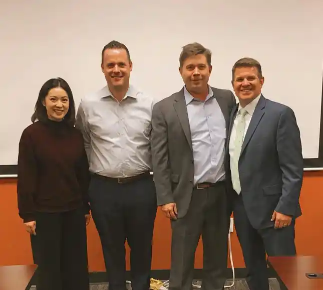 Four professionals posing together in front of orange and white wall at dental practice.